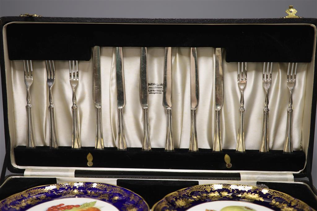 A cased dessert service containing six gilt and fruit decorated plates and a set of knives and forks